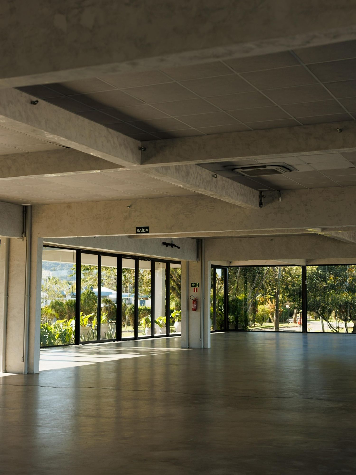 Salão vazio com piso de concreto e janelas para a lagoa